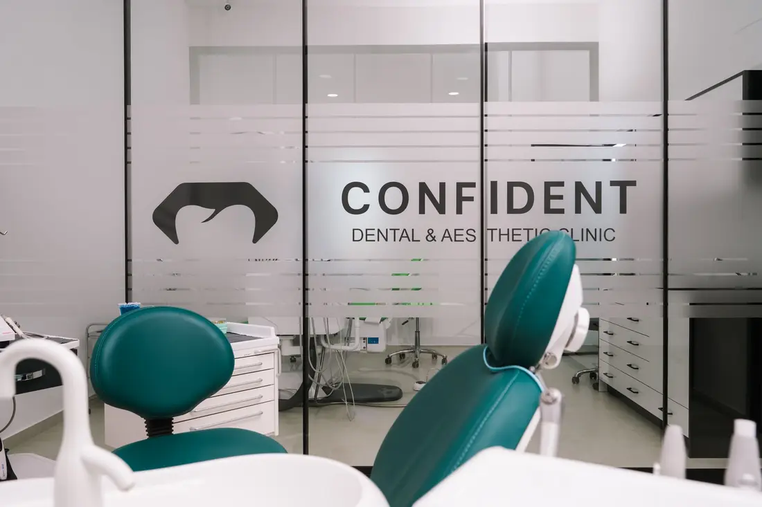 Pogled sa tirkizne stomatološke stolice prema staklenom zidu s logom Confident Dental & Aesthetic Clinic