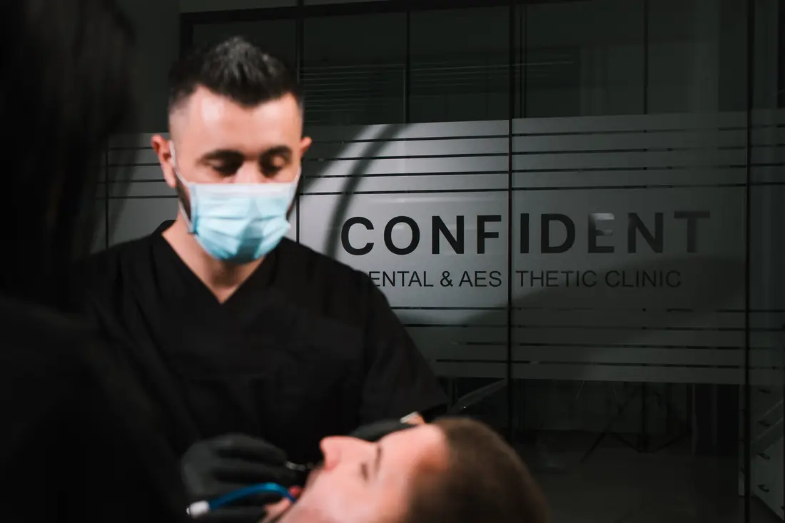 Dr Agron Shabani tokom tretmana pacijenta, iza njega logo Confident Dental & Aesthetic Clinic