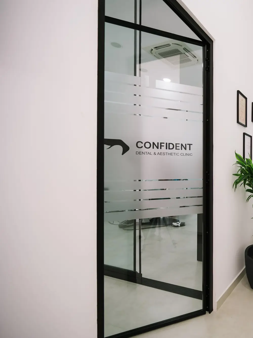 Svijetli hodnik klinike sa staklenim vratima s logom Confident, biljkom i foteljom