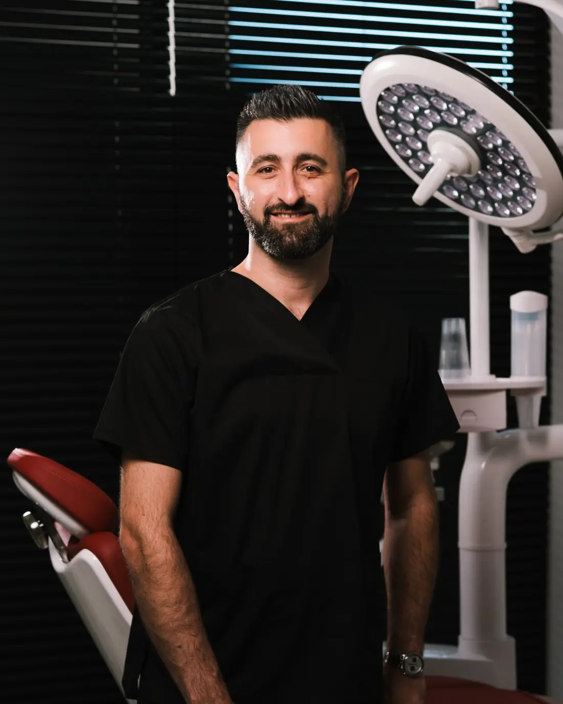 Dr Agron Shabani nasmijan pored stomatološke stolice, ispod operacione lampe