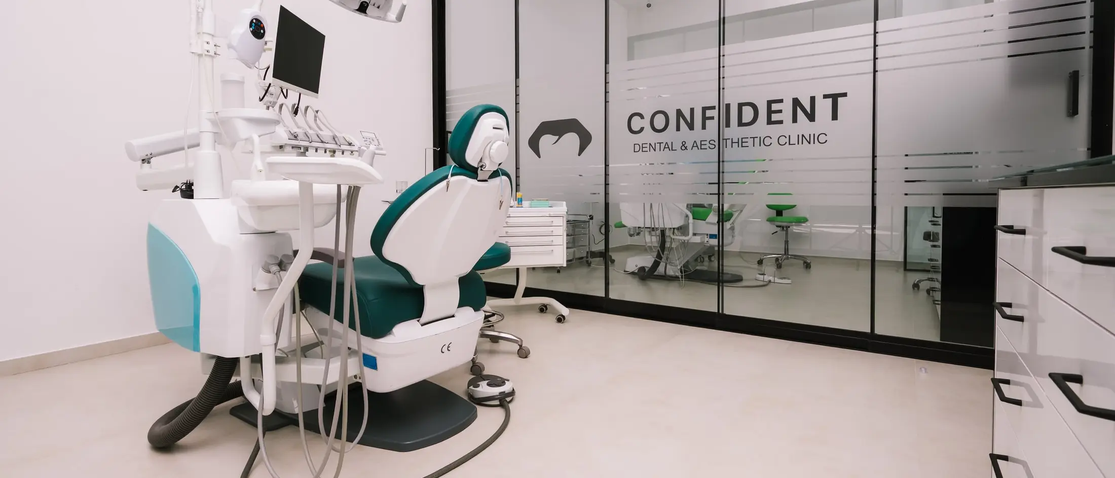 Moderna stomatološka jedinica s tirkiznom stolicom, iza nje stakleni zid s logom Confident